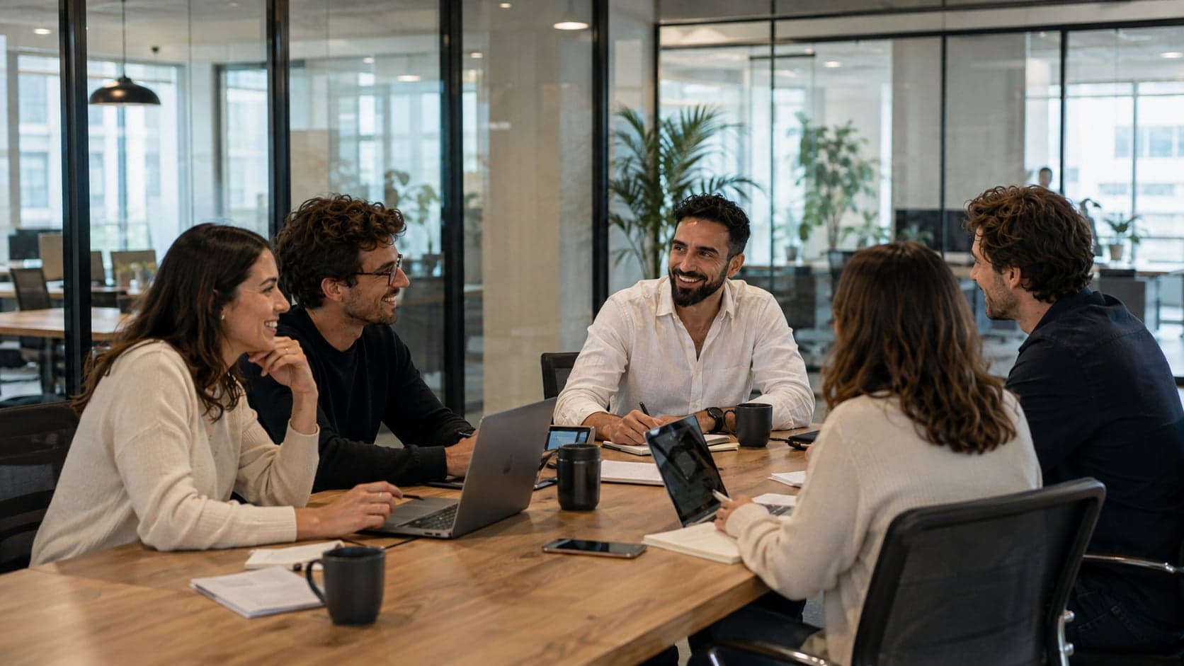 Un equipo trabajando junto a una mesa de reuniones con portátiles y documentos.